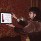 2000 Museum of American Glass Curator Emeritus, Gay Taylor, hanging the American Alliance of Museums Accreditation Certificate.