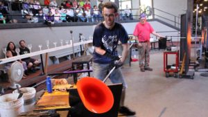 Glass artist spins out a molten disk in front of a gallery audience