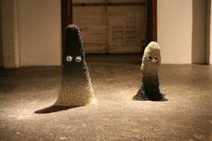 Ghost Sculptures by Christopher Duffy, one ghost with a thicker body and a black to white gradient, and one ghost with a thin body and a white to black gradient. Both ghosts sit side by side indoors with a hard light shining from above them.