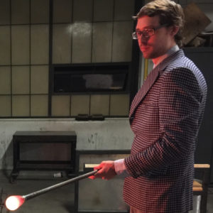 Evan Voelbel in a suit with red hot glass at the end of a blowpipe