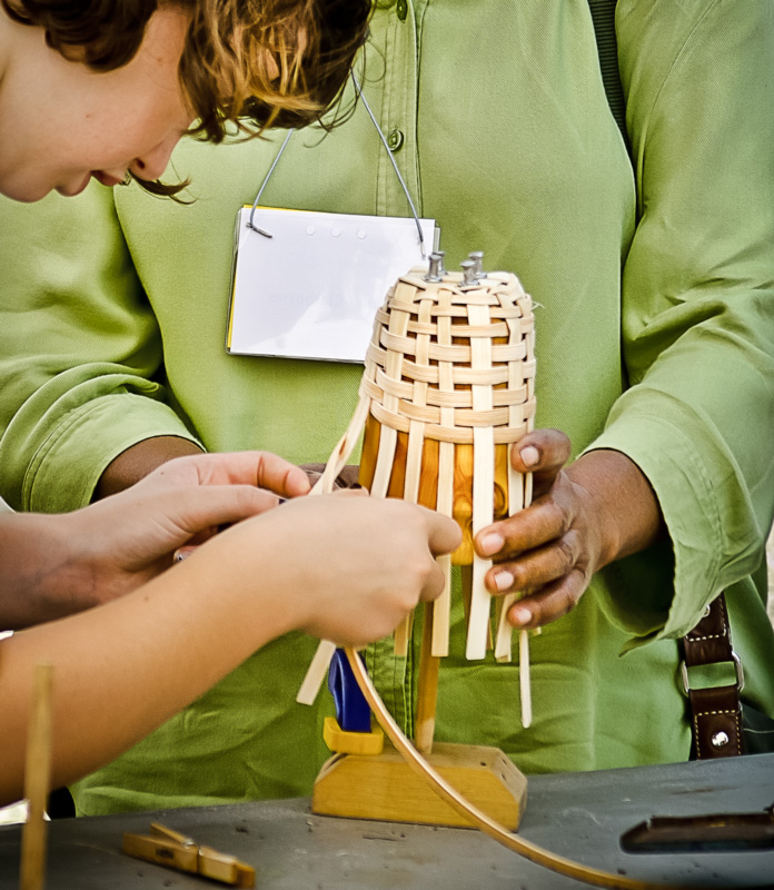 An adult helps a child weave a small basket during the Festival of Fine Craft at WheatonArts