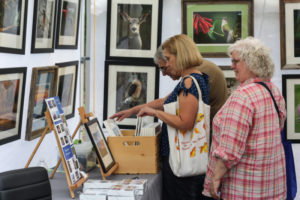 Three people flip through matted prints from a booth at the Festival of Fine Craft at WheatonArts