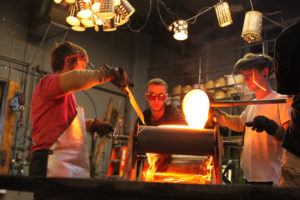 3 artists pouring molten glass into a mold