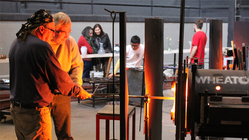 Joe Mattson demonstrating glass blowing to veteran