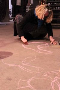 Artist Paula Hayes drawing concepts in pink chalk on the ground