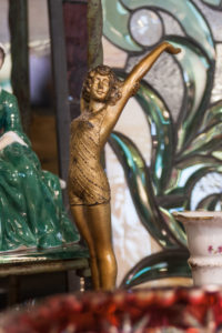 Antique gold painted sculpture of a girl with flowing hair, stretching her arms in a swimsuit.