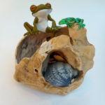 Stylized frog and lizard sculptures sit on a tan shell with a small blue shell inside. Created by Sandy Lehman.