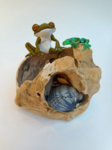 Stylized frog and lizard sculptures sit on a tan shell with a small blue shell inside. Created by Sandy Lehman.