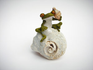 A sculpture of a stylized frog listening to a tiny conch shell. The frog sits on a white spiral shell. Created by Sandy Lehman.