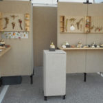A display of Sandy Lehman's work in a booth setting. The sandy color of the walls and display cases unifies the nautical theme.
