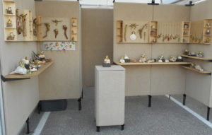 A display of Sandy Lehman's work in a booth setting. The sandy color of the walls and display cases unifies the nautical theme.