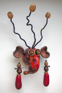Carved gourd face by Robert Lehman with a drooping nose, large ears with dangling red earrings, and three tall, wiry hairs