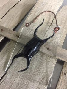 Glass panel with a black design by Scott Manns, displayed on pieces of wood