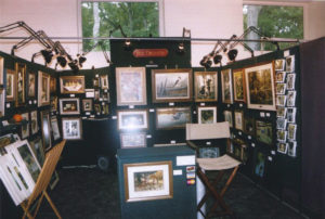 A collection of Ron Orlando's work in a booth setting, each of his pieces hung on a wall and highlighted with a warm light.