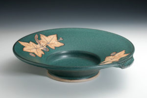 Deep teal plate with detailed tan leaf designs on the lip. Created by Amy Peseller