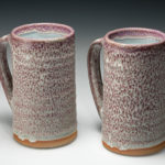 Matching tall white ceramic mugs with pink speckles throughout, as well as a small ring of orange on each bottom. Created by Amy Peseller.