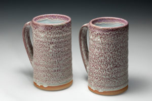 Matching tall white ceramic mugs with pink speckles throughout, as well as a small ring of orange on each bottom. Created by Amy Peseller.