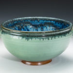 Teal bowl with a green ring around the rim and an orange foot. The inside is a deep cobalt blue. Created by Amy Peseller.