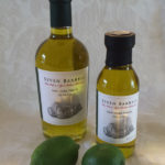 A small and large bottle of "Lime Extra Virgin Olive Oil" from Seven Barrels, one green lime in front of each bottle