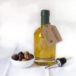 A bottle of extra virgin olive oil from Seven Barrels, with a neighboring small bowl of olives