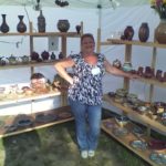 Phyllis Seidner posing at a booth displaying her ceramic art