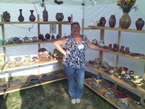 Phyllis Seidner posing at a booth displaying her ceramic art