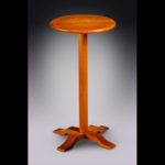 A tall wooden side table with a circle top by Douglas Starry