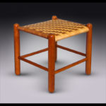 A small wooden footrest with a woven top with alternating tan and brown colors by Douglas Starry