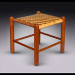 A small wooden footrest with a woven top with alternating tan and brown colors by Douglas Starry