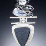 A silver pendant by Willie Trejbal with several faceted black and greystones stacked over two bars and a black triangular stone at the base.