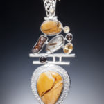 A silver pendant by Willie Trejbal with several faceted orange and brown stones stacked over two bars and an orange teardop shaped stone at the base.