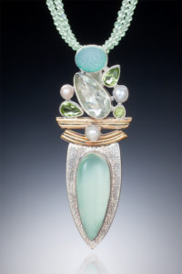 A long silver and gold pendant by Willie Trejbal with several faceted white, blue and green stones stacked over two curved bars and a teal oval stone at the base.