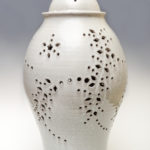 A tall ceramic jar with cut out leaf and flower designs by Phyllis Seidner