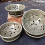 Pale green decorative ceramic bowls and matching saucers, each with cut out holes creating dragonflies and flowers, by Phyllis Seider