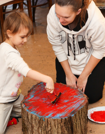 A child rolling red ink onto the rings of pre-cut log, the first step to create a Tree Ring Print.