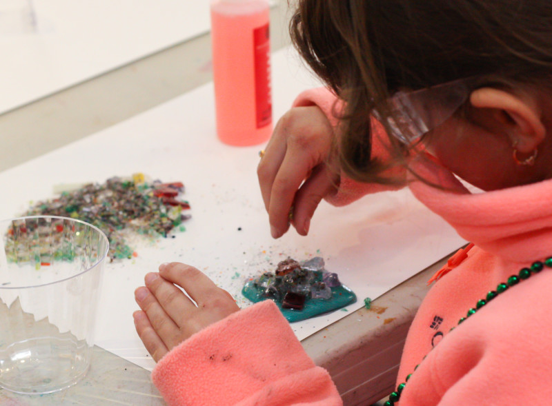 A young girl creating a magnet with glue and glass frit to be fused together later in the kiln.