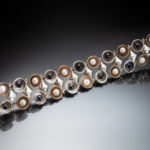 Bracelet by Ricky Boscarino with a row of circles at the top and bottom, each circle alternating between a brass color circle with a white pearl and a silver circle with a black pearl.