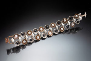 Bracelet by Ricky Boscarino with a row of circles at the top and bottom, each circle alternating between a brass color circle with a white pearl and a silver circle with a black pearl.