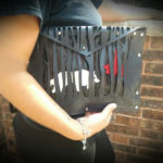 Closeup of a person cradling a black leather purse by Julie Bradley with the design of a wolf stalking little red riding hood, woven through the black branches