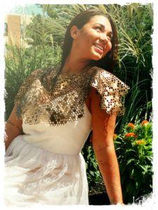 A person leans back in an elegant white dress, looking to the sky. Leather with a cut honeycomb pattern created by Julie Bradley drapes over the model's shoulders and dress