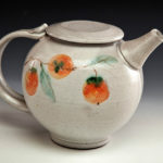 A white ceramic teapot with fruits painted along its side. Created by Pamela Cummings