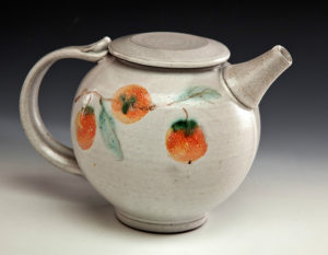 A white ceramic teapot with fruits painted along its side. Created by Pamela Cummings