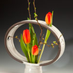 A unique white vase with a ring on top, holding beautiful orange tulips. Created by Pamela Cummings