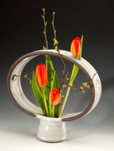 A unique white vase with a ring on top, holding beautiful orange tulips. Created by Pamela Cummings