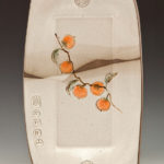 A long white ceramic piece depicting fruits on a branch along its center. Created by Pamela Cummings