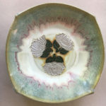 A bowl with muted blues, pinks, and white with three white flowers in the center. Created by Marsha Dowshen