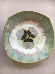 A bowl with muted blues, pinks, and white with three white flowers in the center. Created by Marsha Dowshen