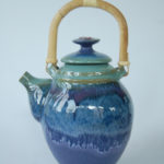 A rich navy teapot with a tan handle and tan foot. Created by Marsha Dowshen