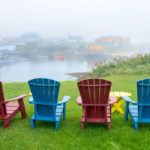 Photograph taken by James Evangelista of four Adirondack chairs on lush green grass, overlooking a foggy river.