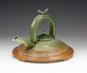 Wide, flat teapot painted tawny to green from bottom to top with a small lid, large handle, and spout. Created by Stephen Fabrico.